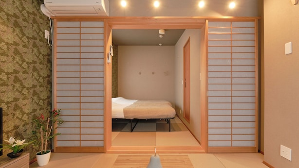 A traditional Japanese-style room with tatami flooring, a low bed, sliding shoji doors, and a small potted plant. - Ryokan Zen Asagaya by Tranova (Tokyo)