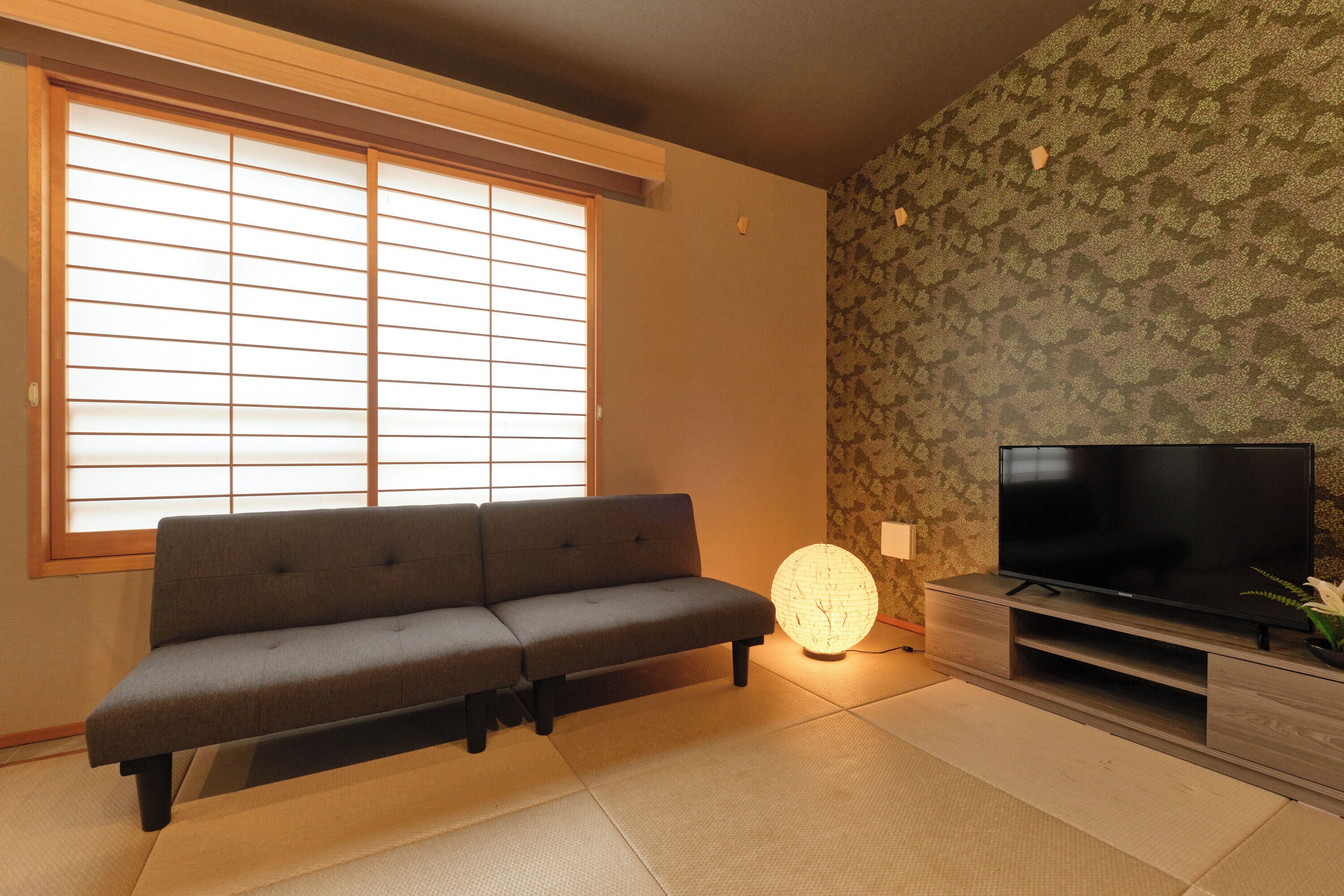 Un salón con sofá, televisión, suelo de estequilla y ventana con pantalla shoji.