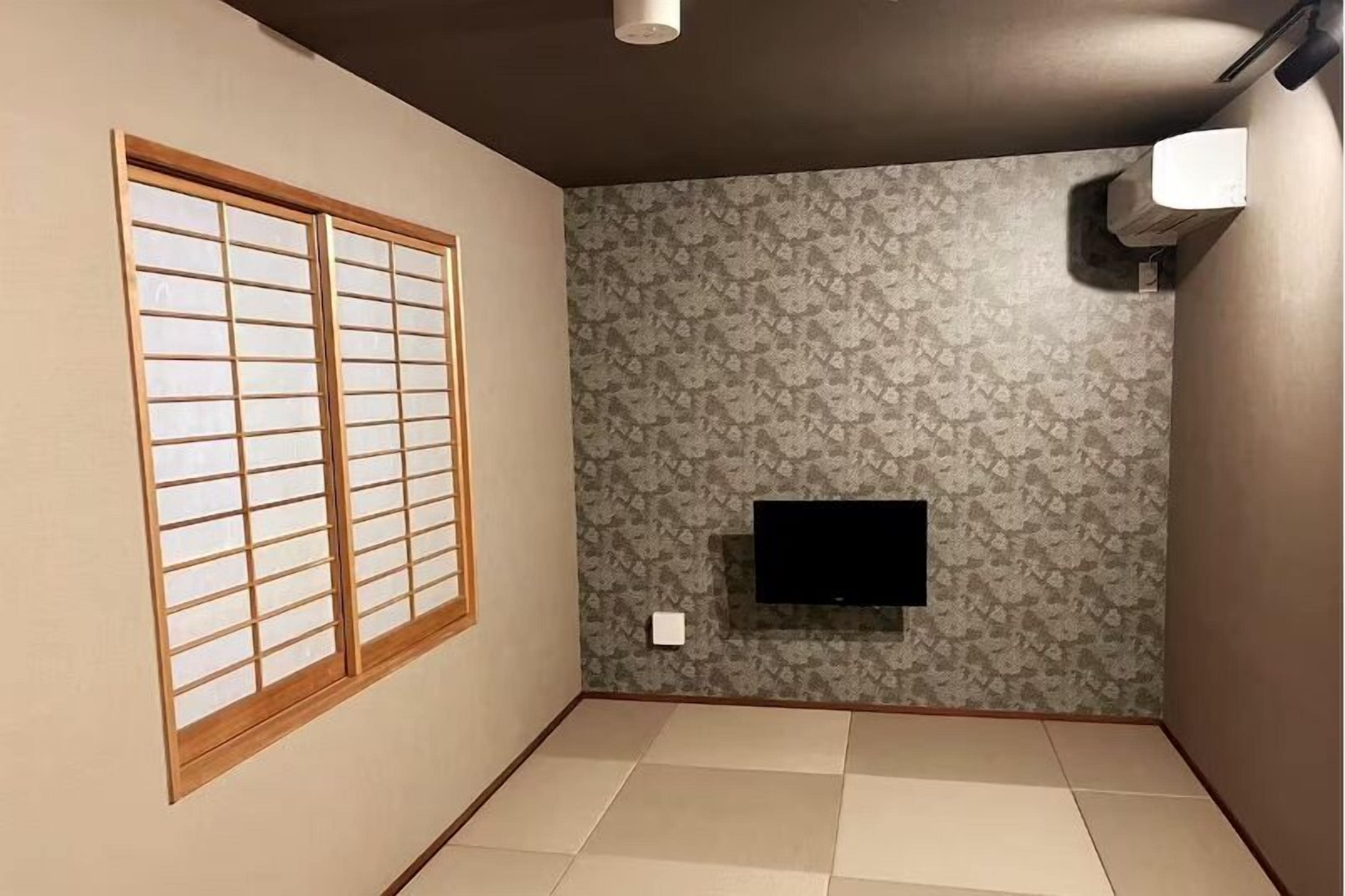 A room with tatami flooring, a sliding shoji screen, a patterned wallpaper, and a mounted TV.