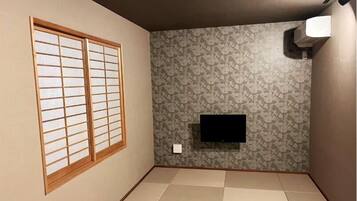 A room with tatami flooring, a sliding shoji screen, a patterned wallpaper, and a mounted TV.