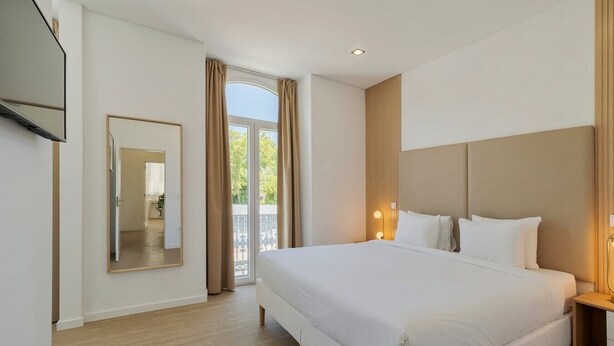 Une chambre d’hôtel avec un grand lit, un téléviseur fixé au mur et une porte-fenêtre coulissante donnant sur un espace extérieur.
