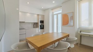 Une cuisine moderne avec des meubles blancs, une table à manger en bois et un four encastré.