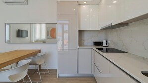Une cuisine moderne avec des meubles blancs, une table à manger en bois et un micro-ondes encastré.