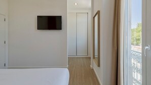 Une chambre d’hôtel avec un lit, un téléviseur fixé au mur, un grand miroir et une fenêtre avec des rideaux.