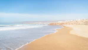 Una playa con cielo despejado, orilla arenosa y edificios a lo lejos.