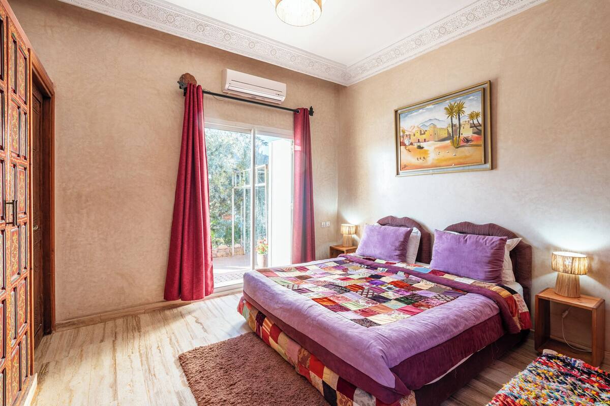 Un dormitorio con una cama grande, dos lámparas de noche, un cuadro y una ventana con cortinas.
