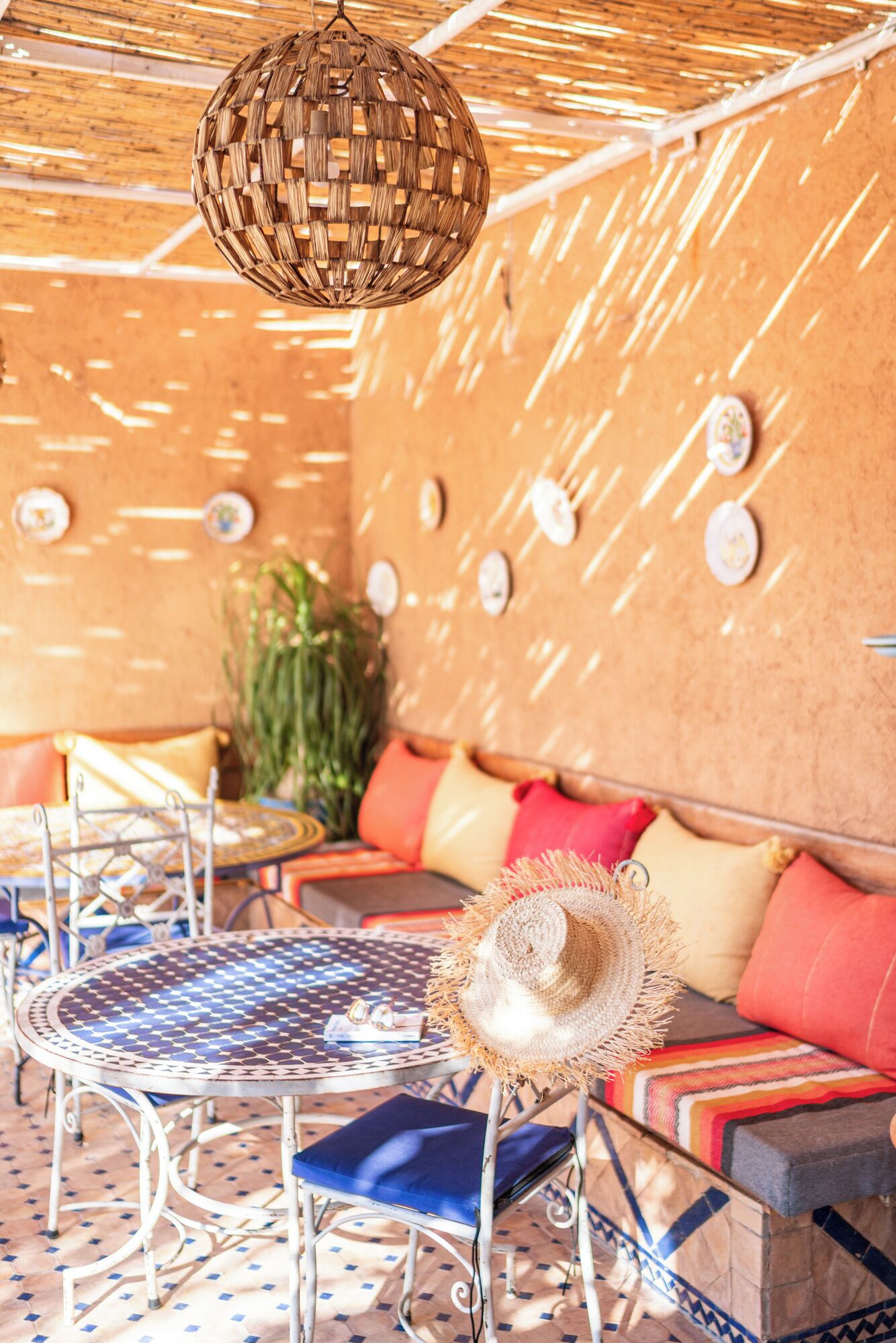 A cozy lounge area with a woven ceiling light, patterned cushions, and a round metal table.