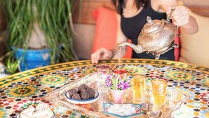 Una persona sirve té desde una tetera metálica tradicional sobre una mesa marroquí colorida.