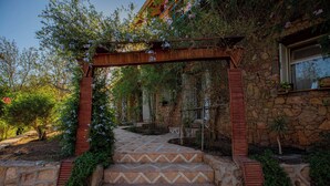 Un edificio de piedra con un porche de madera, escalones que conducen a un jardín y una ventana con plantas.