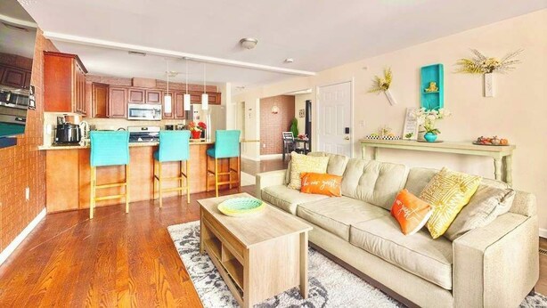 Een moderne keuken met een centraal eiland, een eethoek met stoelen, een bank met kussens en een decoratieve plank met planten.