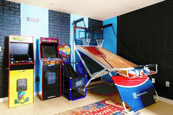 Una habitación con máquinas de videojuegos, una canasta de baloncesto y una alfombra roja.