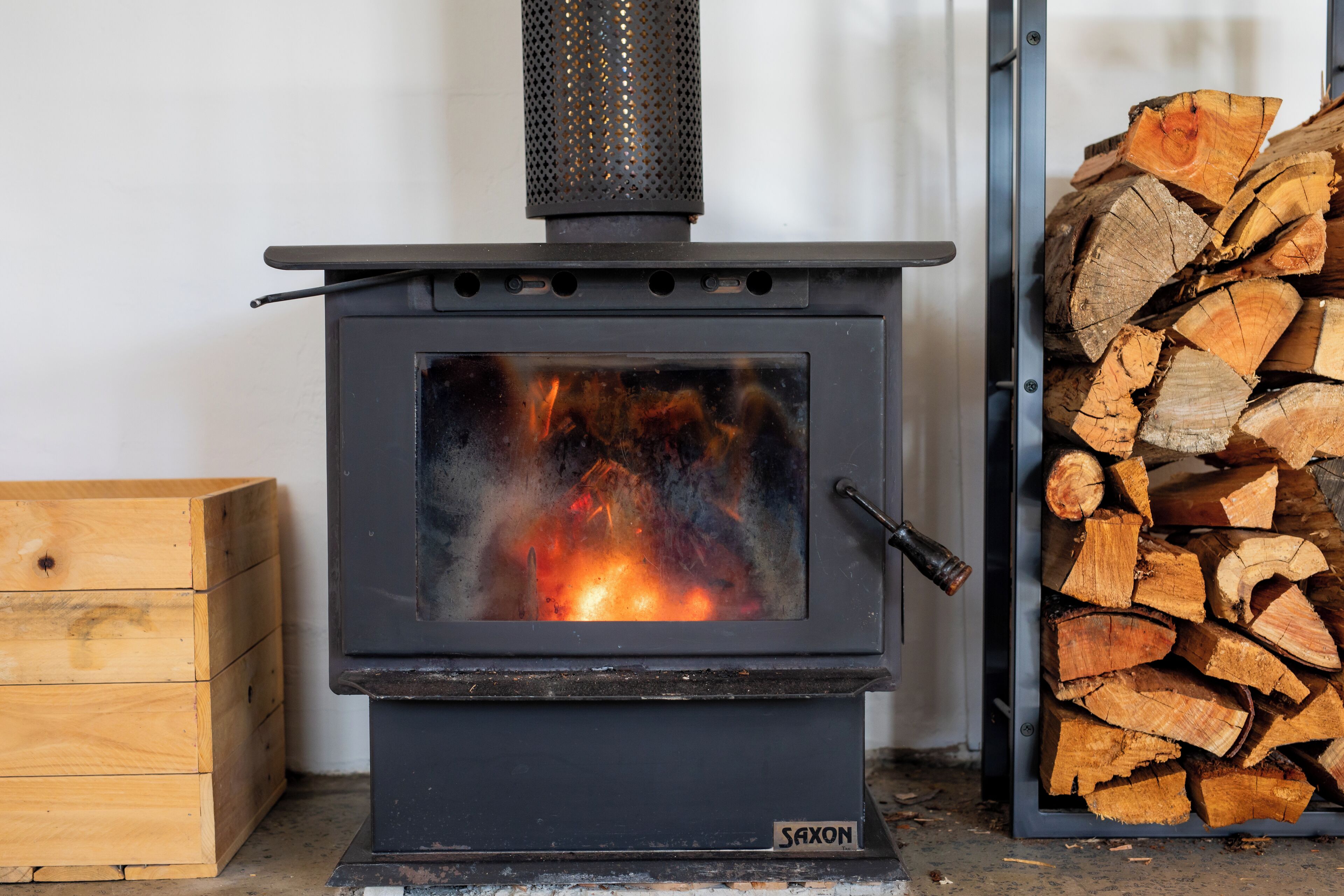A wood-burning stove with a visible fire, a metal grate, and a stack of firewood to the right.