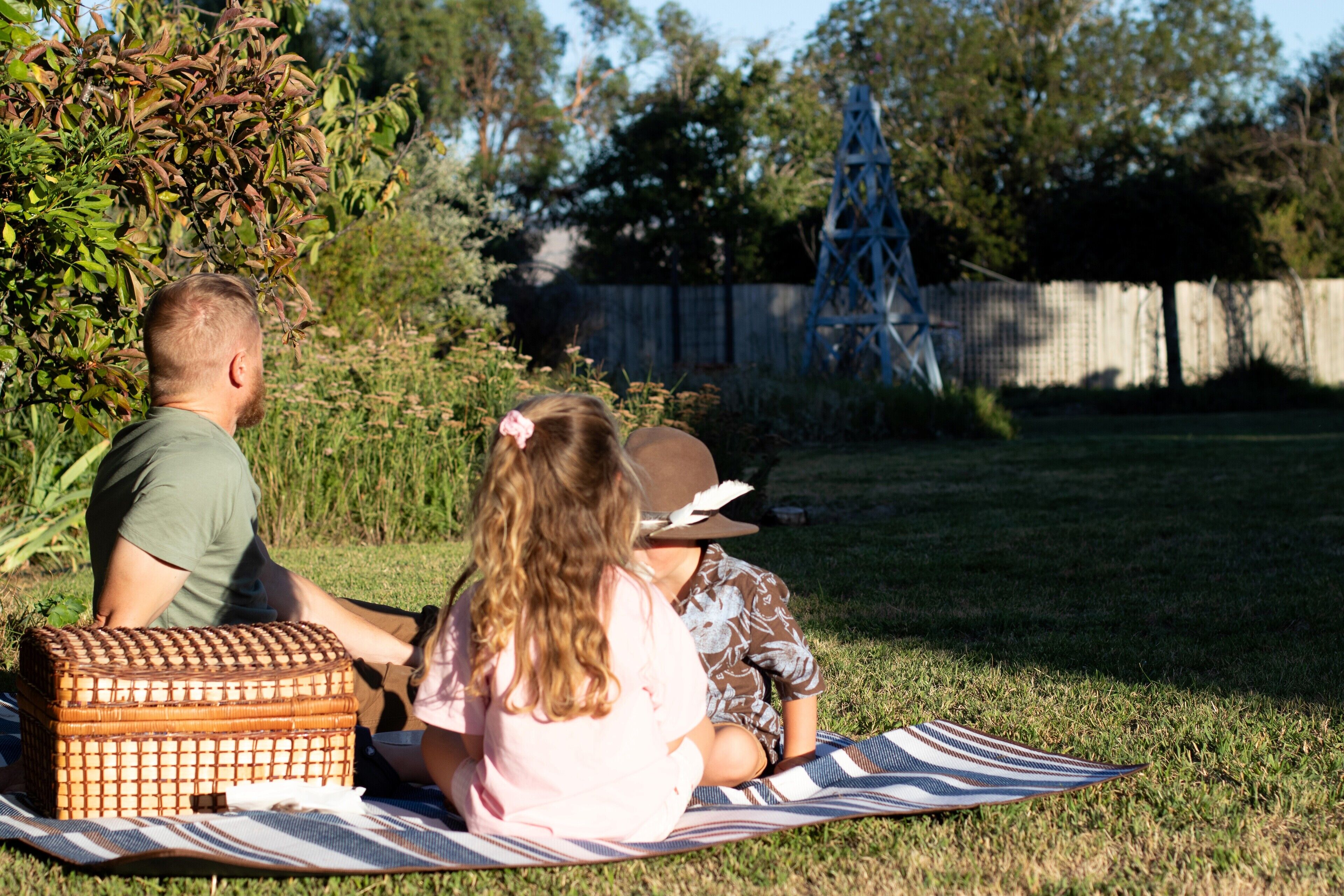 A family of three on a picnic blanket in a grassy backyard.