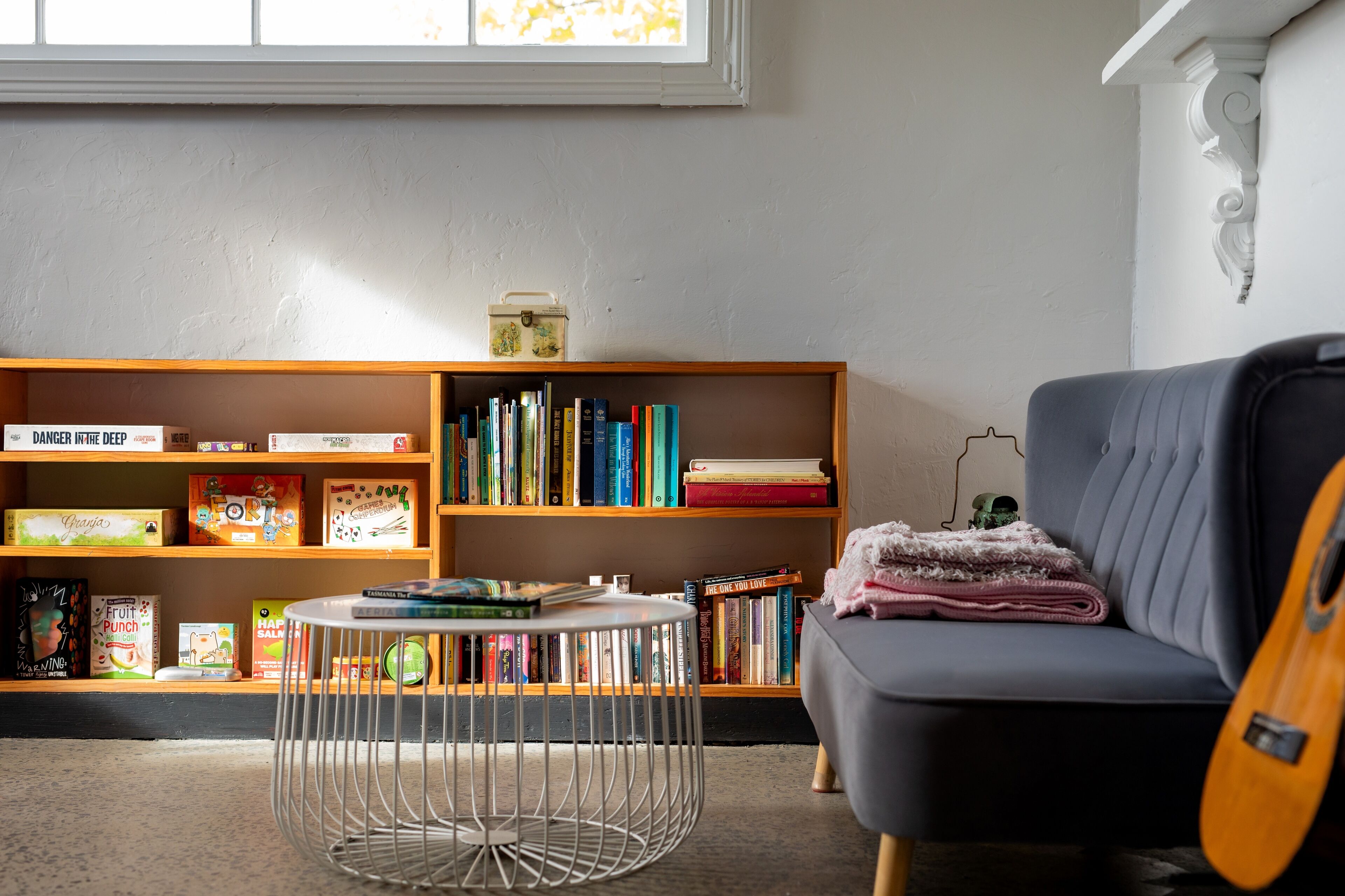 A cozy room with a bookshelf, a grey sofa, a round metal table, and a guitar.