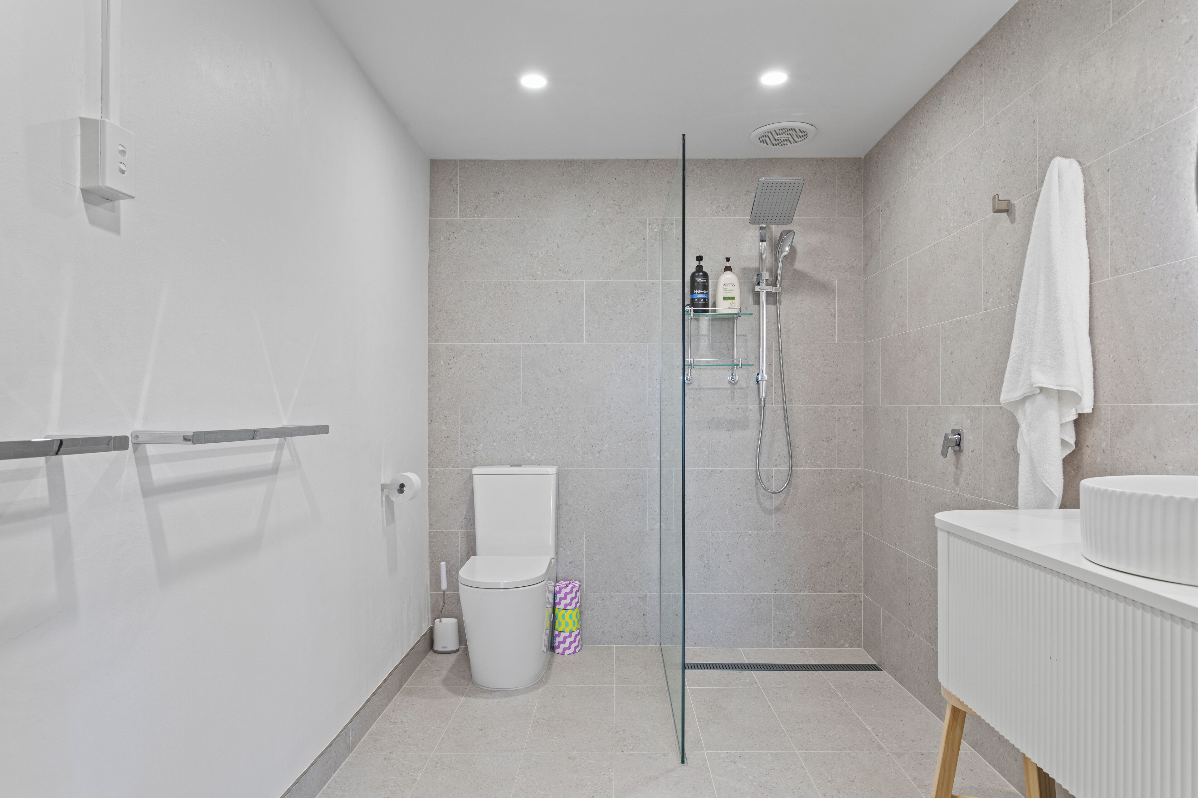 A modern bathroom with a glass-enclosed shower, a white toilet, and a white sink with a towel hanging on the wall.