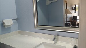 A bathroom with a white sink, a mirror, and a towel rack. - Brooks City Executive Inn (San Antonio)