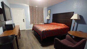 A hotel room with a bed, a desk, a chair, a dresser, a mirror, a door, and a window with curtains. - Brooks City Executive Inn (San Antonio)
