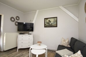 A living room with a white TV, a painting, a sofa, and a small table.