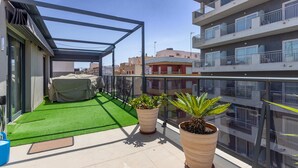 A rooftop terrace with artificial grass, a covered seating area, and potted plants.