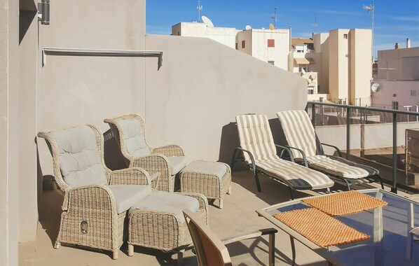 A rooftop terrace with wicker lounge chairs and a table, overlooking a cityscape.