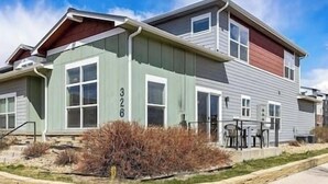 A two-story residential building with a green and gray exterior, a visible number '326', and a small patio area with outdoor furniture. - Cozy townhome in old town north dogs, Bikes. (Fort Collins)