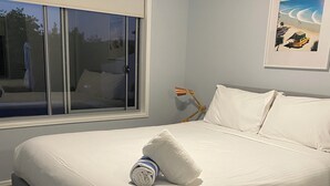 Ein ordentlich bezogenes Bett mit weißen Leinentüchern, einem aufgerollten Handtuch und einem einzelnen Kopfkissen.