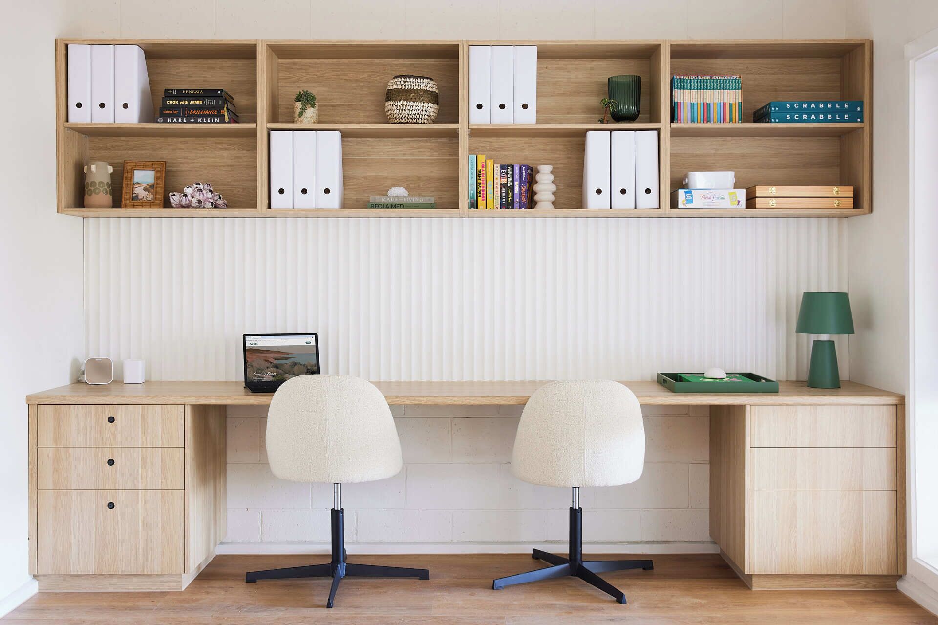 Un espace de travail comprenant un bureau en bois, deux chaises, un ordinateur portable et des étagères remplies de livres et d’objets décoratifs.