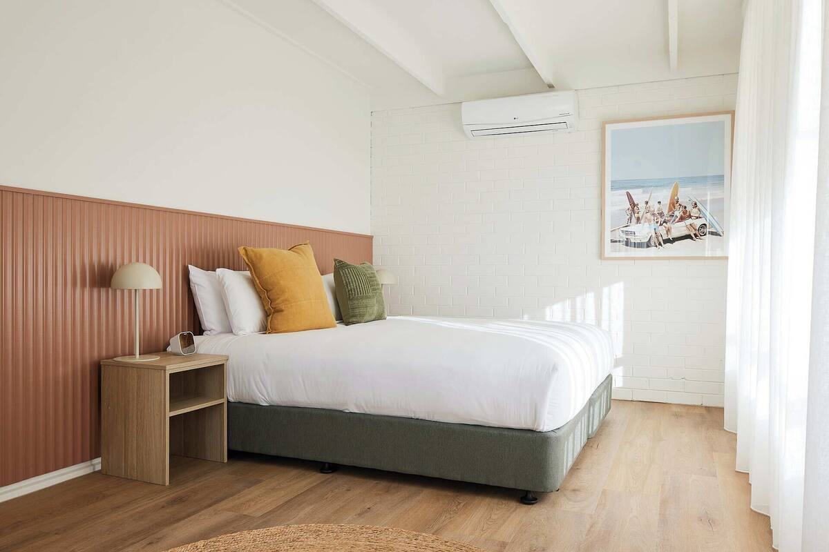 A bedroom with a bed, bedside table, lamp, and a painting on the wall.