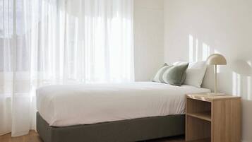 A bedroom with a bed, a nightstand, a lamp, and sheer curtains.
