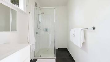 Un baño moderno con cabina de ducha de vidrio, paredes blancas y suelo de baldosas negras.
