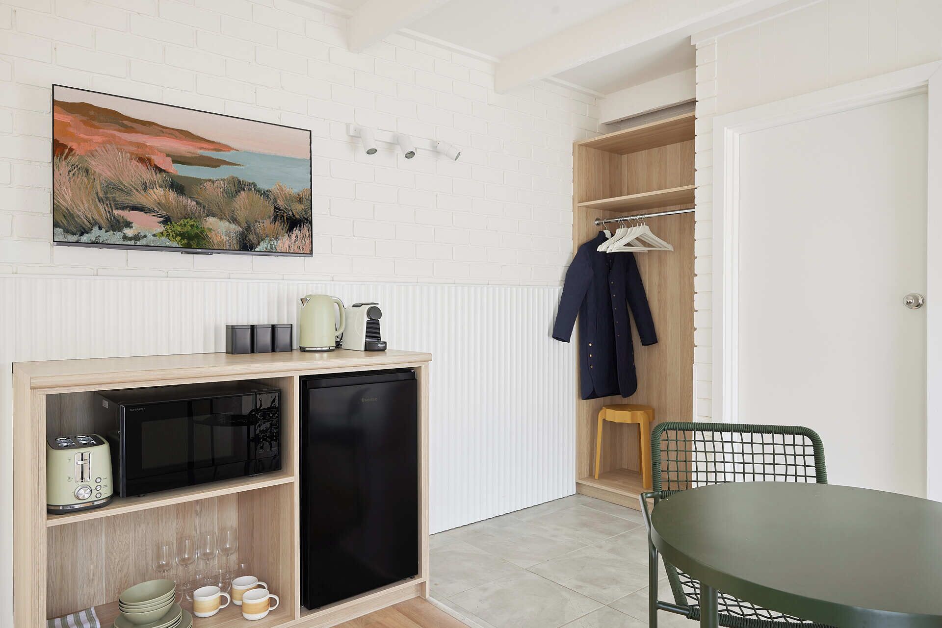 A compact kitchen with a microwave, toaster, and kettle, a wooden cabinet, and a dining area with a table and chair.