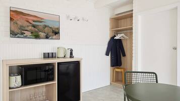 A compact kitchen with a microwave, toaster, and kettle, a wooden cabinet, and a dining area with a table and chair.