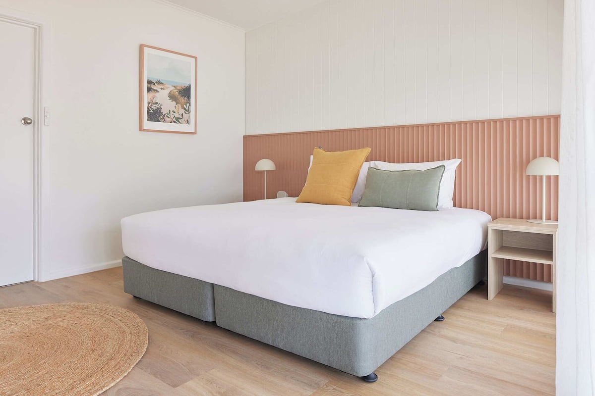A neatly arranged bedroom with a bed, bedside lamps, and a framed picture on the wall.