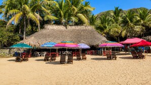 Una playa con estructuras de techo de paja, sillas de madera y sombrillas.