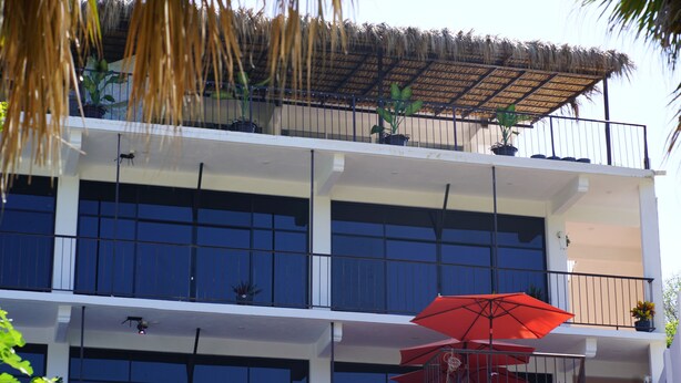 A multi-story building with balconies, potted plants, and a red umbrella. - Casa Esperanza (San Pedro Pochutla)