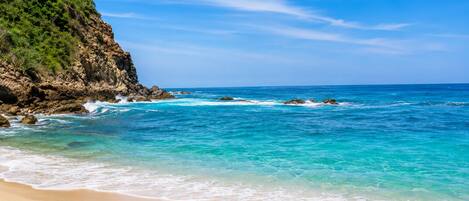 A beach with clear turquoise waters, a sandy shore, and a rocky cliff.