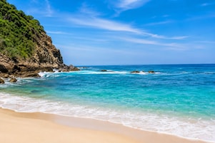 Una playa con aguas turquesas cristalinas, una orilla de arena y un acantilado rocoso.