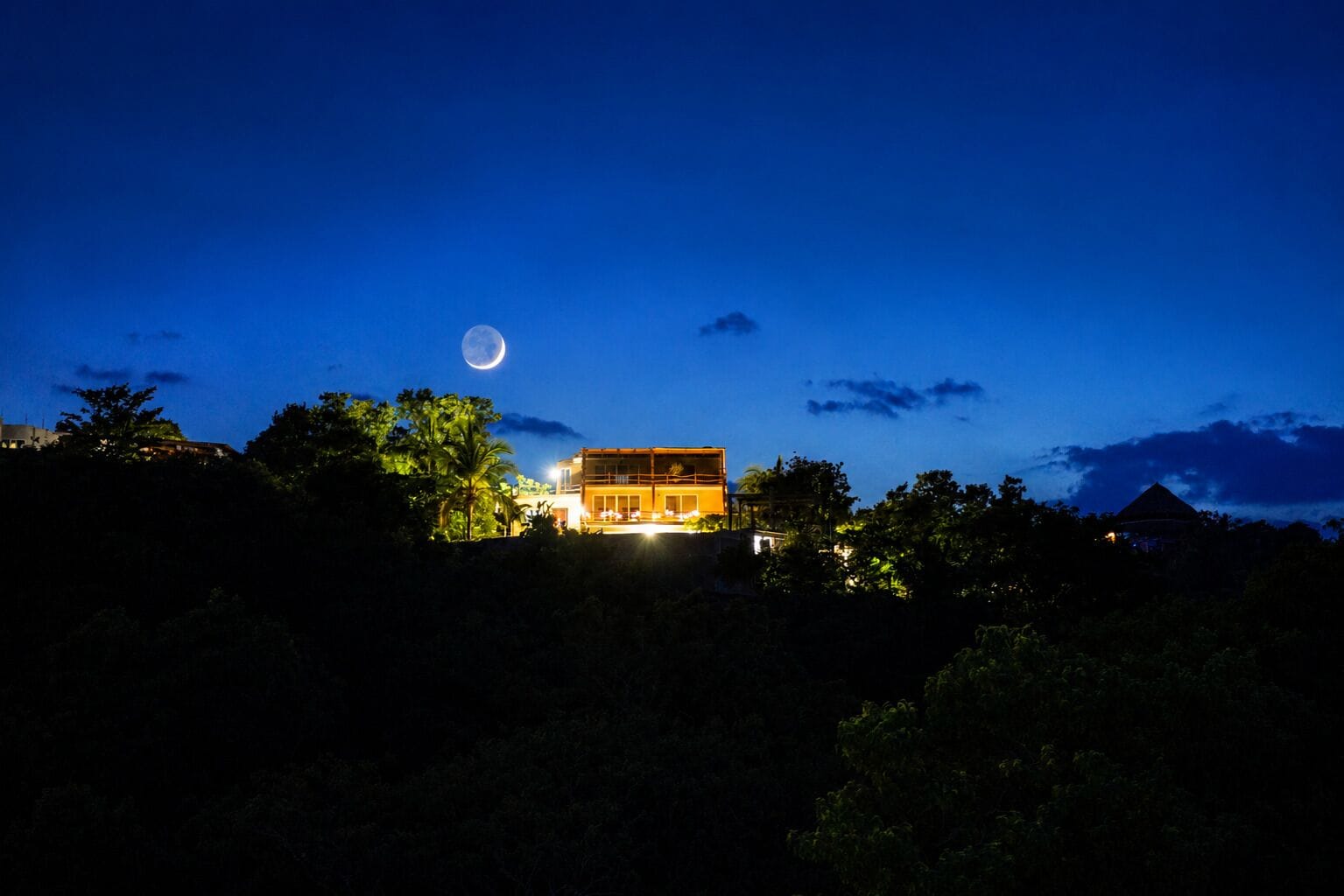 Un edificio con balcón, rodeado de árboles, bajo un cielo nocturno con luna visible.