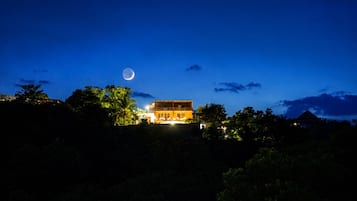 Un edificio con balcón, rodeado de árboles, bajo un cielo nocturno con luna visible.
