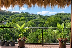 Un balcón con vistas a un paisaje verde exuberante, plantas en macetas y un techo de paja.