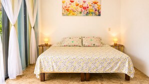 Un dormitorio con una cama, dos mesitas de noche con lámparas, un cuadro en la pared y cortinas en la ventana.