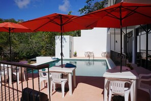 A poolside area with white plastic chairs and tables, red umbrellas, and a clear blue sky. - Casa Esperanza (San Pedro Pochutla)