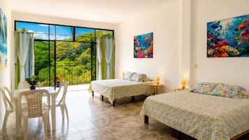 Una camera d'hotel con due letti, un balcone con vista sul verde, un tavolo da pranzo con sedie e opere d'arte alle pareti.