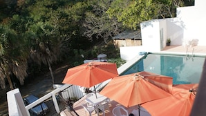 A rooftop pool area with two white tables and orange umbrellas, surrounded by lush greenery. - Casa Esperanza (San Pedro Pochutla)