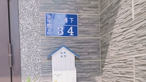 Un letrero azul con texto blanco que indica la habitación número 34, un adorno de casa para pájaros blanca y follaje verde con flores rojas.