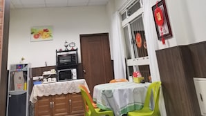 Una habitación con una mesa, sillas, microondas, refrigerador y una ventana decorada.
