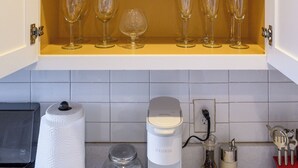 Et køkken med åbne skabe fyldt med hvide tallerkener, klare drikkeglas og en hvid elkedel.