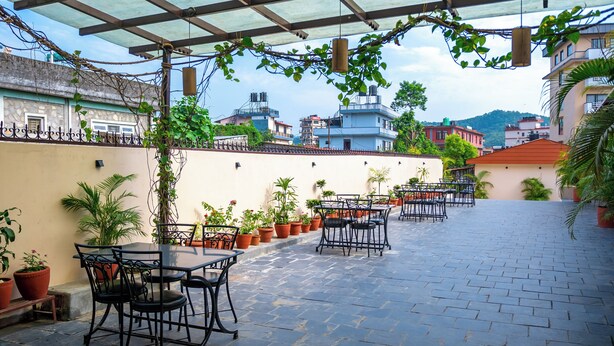 A covered outdoor seating area with tables and chairs, surrounded by potted plants and overlooking a cityscape. - Hotel Rudrakshya Pokhara (Pokhara)