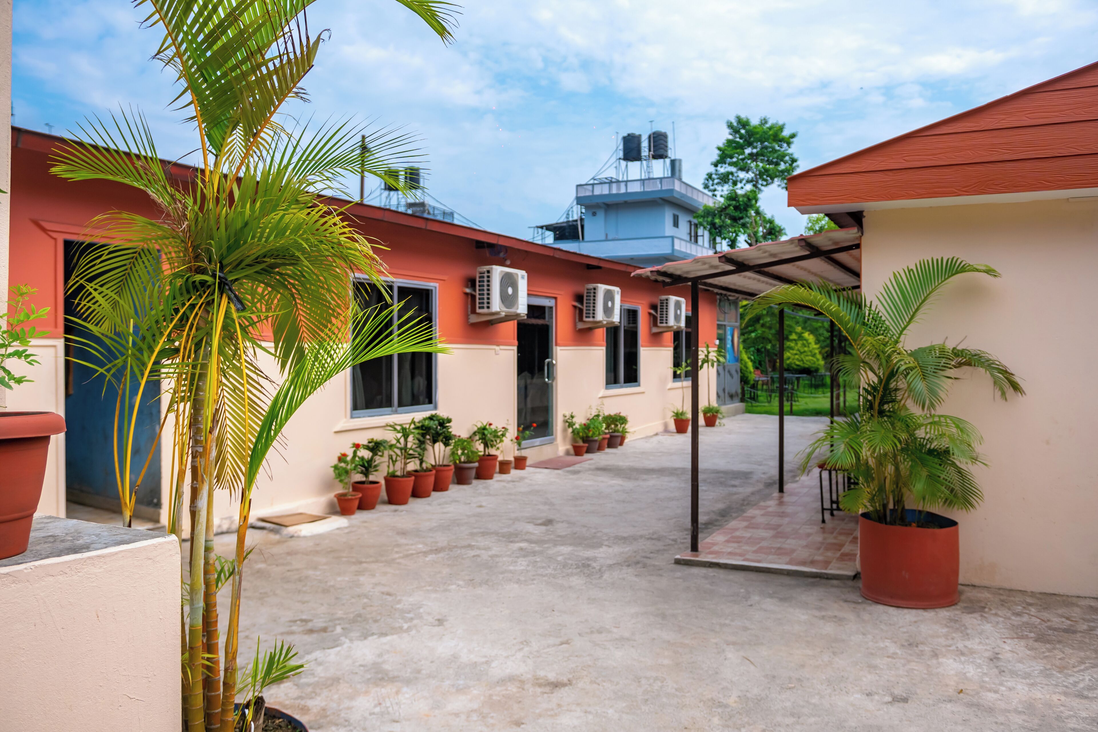 A courtyard with potted plants, air conditioning units, and a building with a red roof.