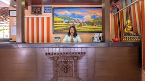 A hotel reception desk with a digital clock, a painting of a mountainous landscape, and a Buddha statue. - Hotel Rudrakshya Pokhara (Pokhara)